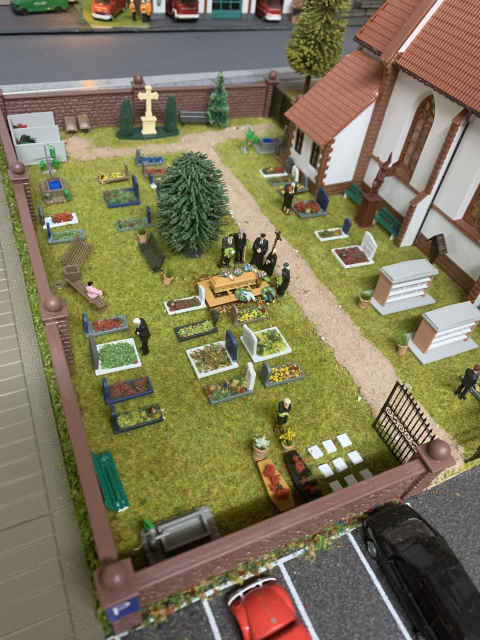 Friedhof mit Gräbern sowie einer gerade stattfindenden Beerdigung