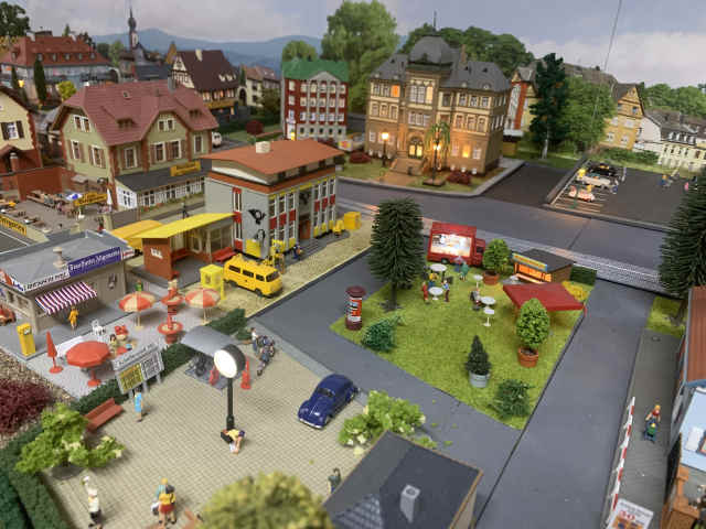 v.l.n.r.: Gasthaus mit Biergarten, Postamt und Rathaus. Im vorderen rechten Bereich steht ein Würstchen- sowie ein Hähnchenstand.