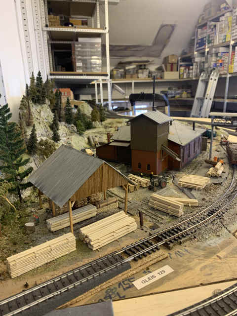 Sägewerk von vorne mit Holzstapeln davor entlang des Gleises
