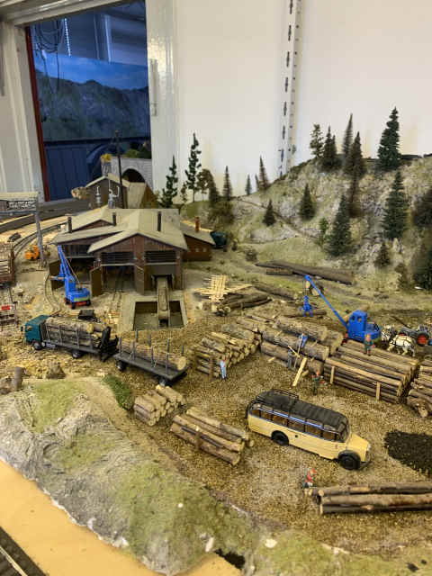 Sägewerk von hinten mit gelagerten Baumstämmen und zwei Kränen 